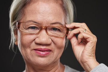 Face of aged Vietnamese woman adjusting her glasses