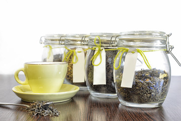 tea in spoon, glass jars and cup on wooden table with white background