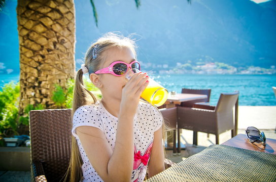 Adorable little girl drinking juice for breakfast in outdoor cafe
