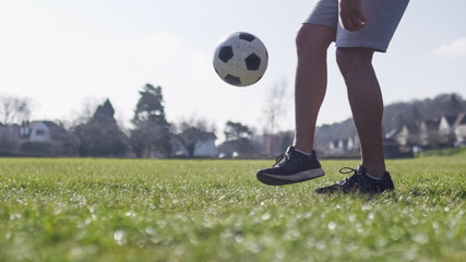 Football player doing kick ups in the park on a bright day