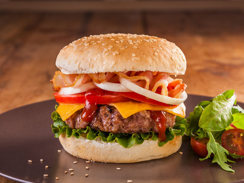 A juicy charcoal broiled hamburger with bacon, onion rings, tomato, cheddar cheese and vegetables.