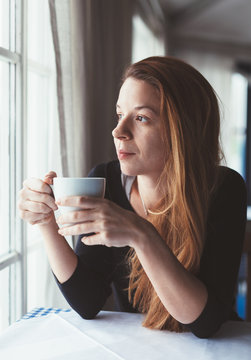Young woman drinking coffee by the window
