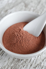 Red cosmetic clay powder in a small white bowl  close up