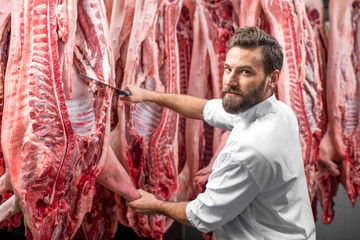 Fototapeta na wymiar Handsome butcher cutting pork carcasse at the meat manufacturing
