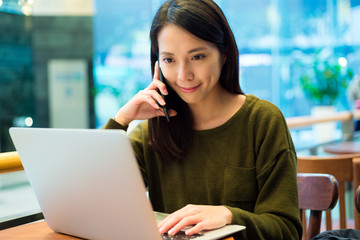 Woman working on laptop computer and talk to cellphone