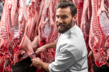 Obraz premium Handsome butcher cutting pork carcasse at the meat manufacturing