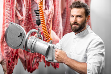 Handsome butcher cutting pork carcasse with electric hand saw at the meat manufacturing