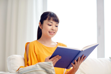 Naklejka premium smiling young asian woman reading book at home