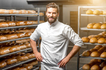 Portrait of handsome baker at the bakery with breads and oven on the background - obrazy, fototapety, plakaty