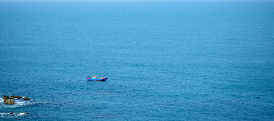 Far way small lonely boat in the blue sea. Landscape of Eo Gio cape, Binh Dinh province, Vietnam.