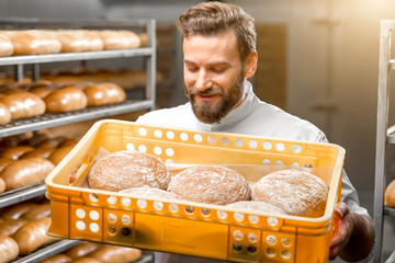 Handsome baker holding box full of freshly baked buckweat breads at the manufacturing - Powered by Adobe