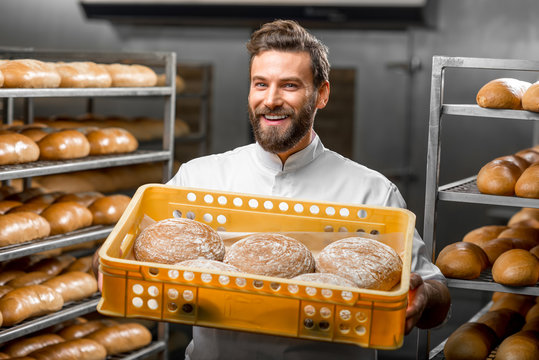 Handsome baker holding box full of freshly baked buckweat breads at the manufacturing