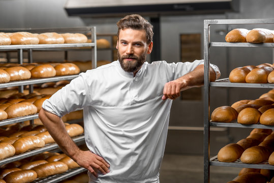 Portrait of handsome baker at the bakery with breads and oven on the background