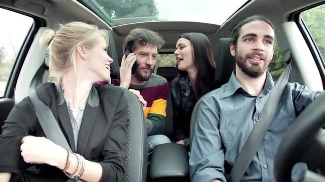 Two women and men in car talking with friend on the phone laughing