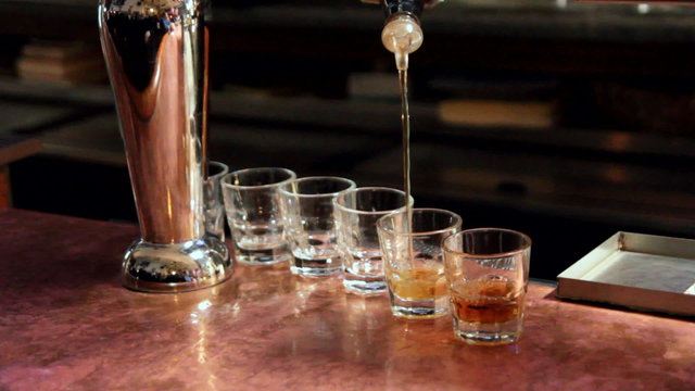 Bar tender pouring whiskey into six shot glasses.