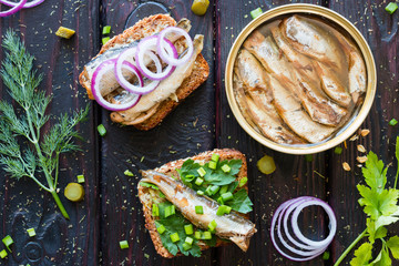 grain bread with sardines and greens next to the bank sprats  on a black background with dill and parsley