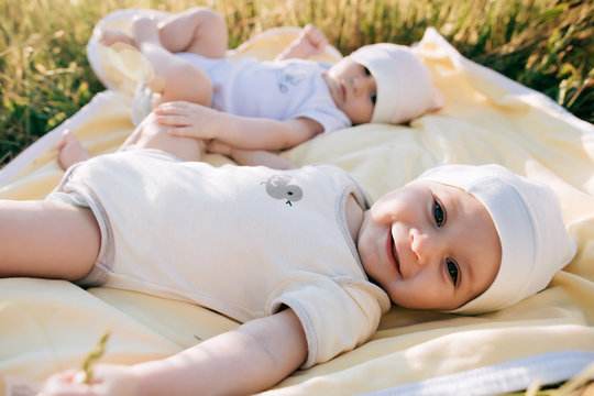Funny twins sisters newborn babies lying on grass in summer day