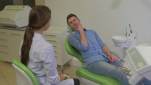 Patient is Talking to Dentist Touching His Jaw Woman Doctor is Sitting Dressed in Lab Coat and Listening to a Patient Dental Clinic Visit to the Dentist