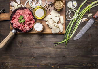 raw ground beef in a small frying pan, on a chopping board with onions, bread, butter and spices on wooden rustic background top view