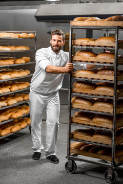 Handsome worker in uniform carrying shelves with bread at the bakery manufacturing