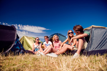 Teenagers sitting on the ground in front of tents