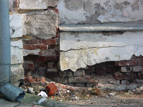 Old dilapidated stucco foundament of building with red bricks in