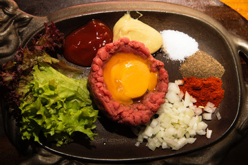 Fresh beef tartar with egg, pickled with spices, onion, ketchup