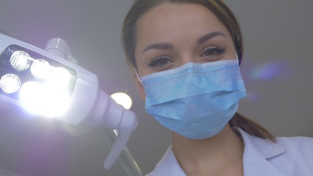 Young Dentist in Mask is Holding a Tools Standing Upon a Patient Turns the Light on Then Off Lab Coat Hands in Gloves Examination in Dental Clinic