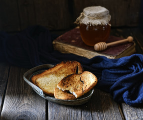 crispy toasts in vintage plate, honey and book on a wooden background