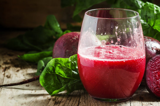 Beetroot smoothie in a large glass, fresh beets with tops, old w