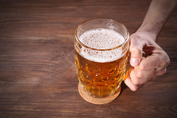 Male hand holding glass of beer on wooden background