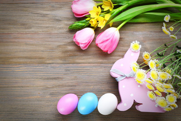 Easter eggs with spring flowers and rabbit on wooden background