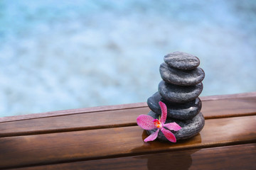 Stack of spa stones with pink orchid on wooden wet bridge