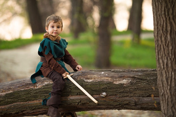 Cute little boy dressed up as a knight playing in the woods with a handmade sword