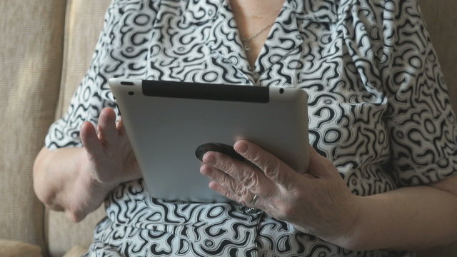 Old woman looks at photos on digital tablet