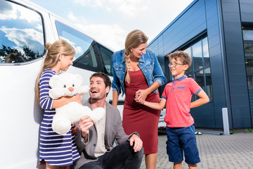 Familie mit Kindern kauft Auto im Autohaus und steht vor dem Neuwagen