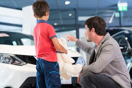 Vater mit Sohn im Autohaus kauft Auto, im Verkaufsraum schauen sie Neuwagen an
