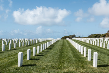Fototapeta na wymiar Grave markers in rows with a cloudy blue sky at Fort Rosecrans National Cemetery in San Diego, California. 