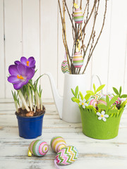 Ostereier, lila Krokus und Osterstrauch  vor einer Holzwand 