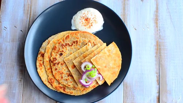 Woman hand serve a platter of Paratha flatbread with red and spring onion and yogurt. Food background and texture