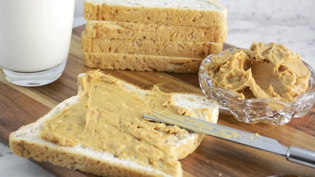 Peanut Butter on fresh slice of bread with glass of milk, zoom in close up on peanut butter.
