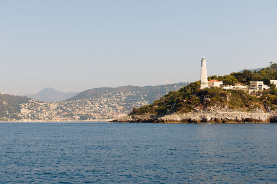 Color DSLR stock image of a lighthouse and houses along the Mediterranean coast of the French Riviera near Nice, France. Horizontal with copy space for text