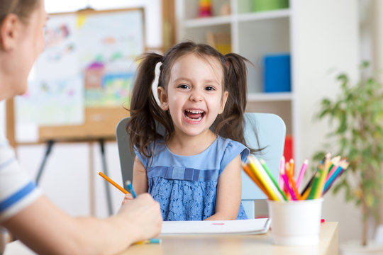 Child little girl laughing, painting colorful pencils at her playtable