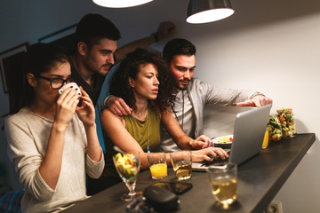 Friends sitting together in living room and watching movie on on laptop  and chatting