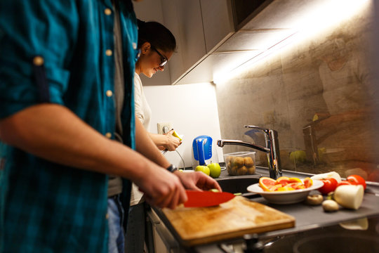 Young couple in kitchen preparing together  vegetarian meal.Preparing fruit salad.Evening.