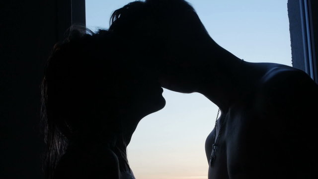 man and woman kissing near a window