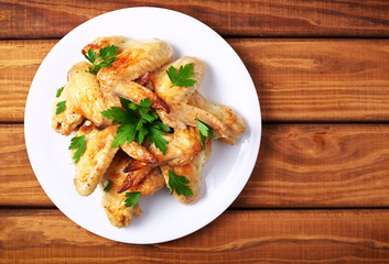 Plate with baked chicken wings and parsley on a wooden background