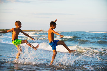 Two boys adolescence playing in the sea water splashing feet wat