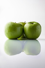 Three green fresh ripe apples on white background with reflection from side vertical composition
