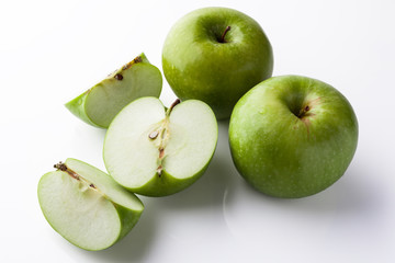 Two whole green apples and one sliced on white background directly from side high angle with reflection